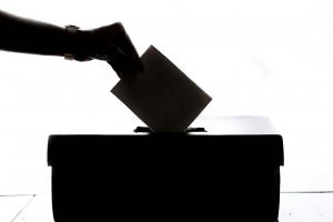 silhouette of a hand dropping a ballot into a voting box